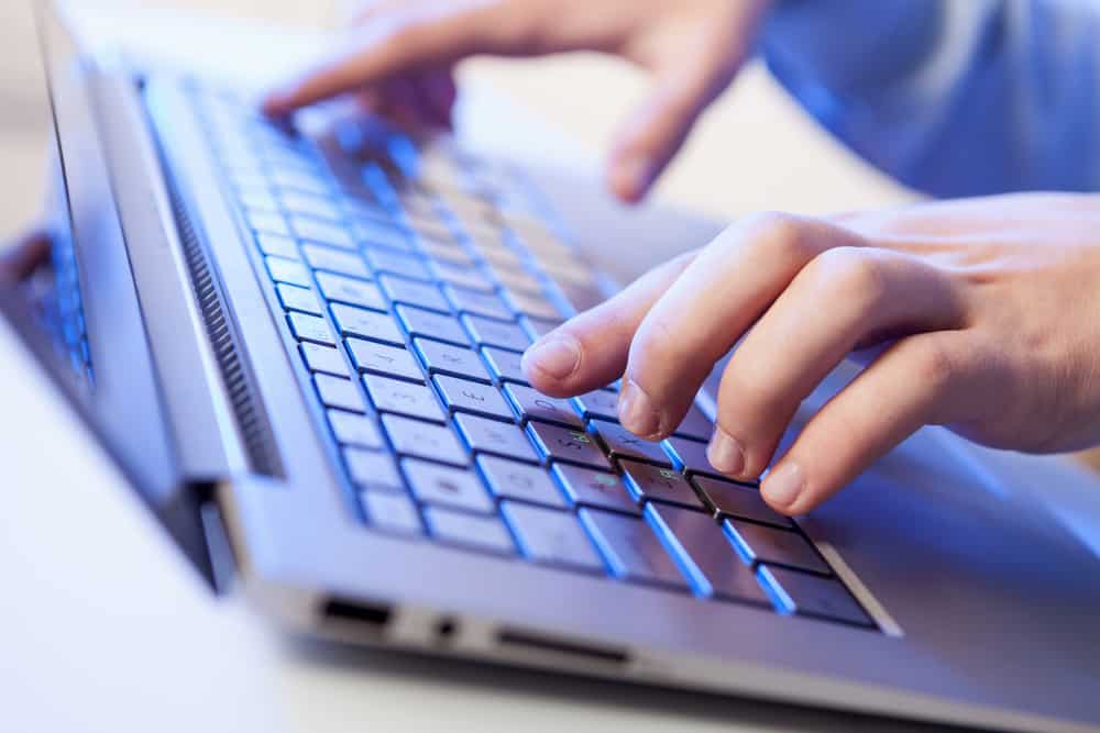 Click! Hands of a man on a keyboard with blue backlighting.